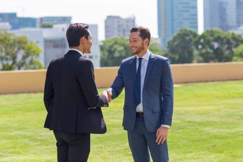 An international CEO and a Guinean entrepreneur shaking hands in front of the headquarters, symbolizing the success of Yes Invest in Guinea partnerships.