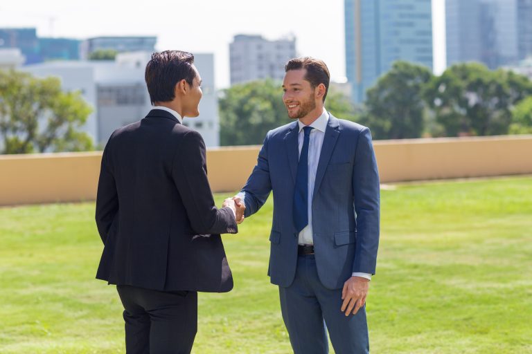 Two Smiling Business Men Shaking Hands Outdoors - YES! INVEST in GUINEA An international CEO and a Guinean entrepreneur shaking hands in front of the headquarters, symbolizing the success of Yes Invest in Guinea partnerships.